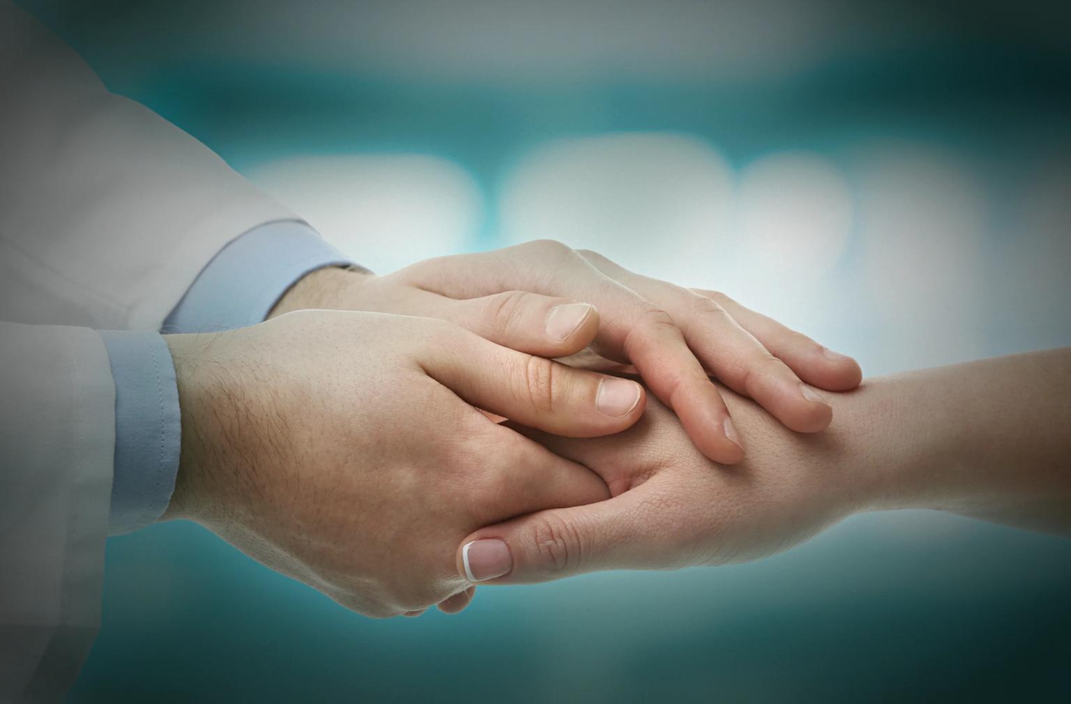 A clinician gently holding a patient's hand in a consultation setting.